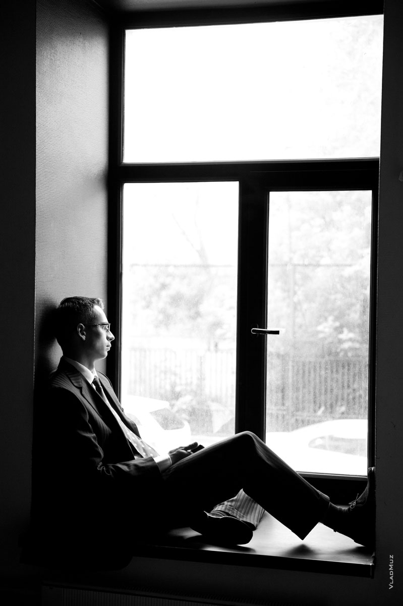 Фото мужчины в костюме у окна, сидя на подоконнике