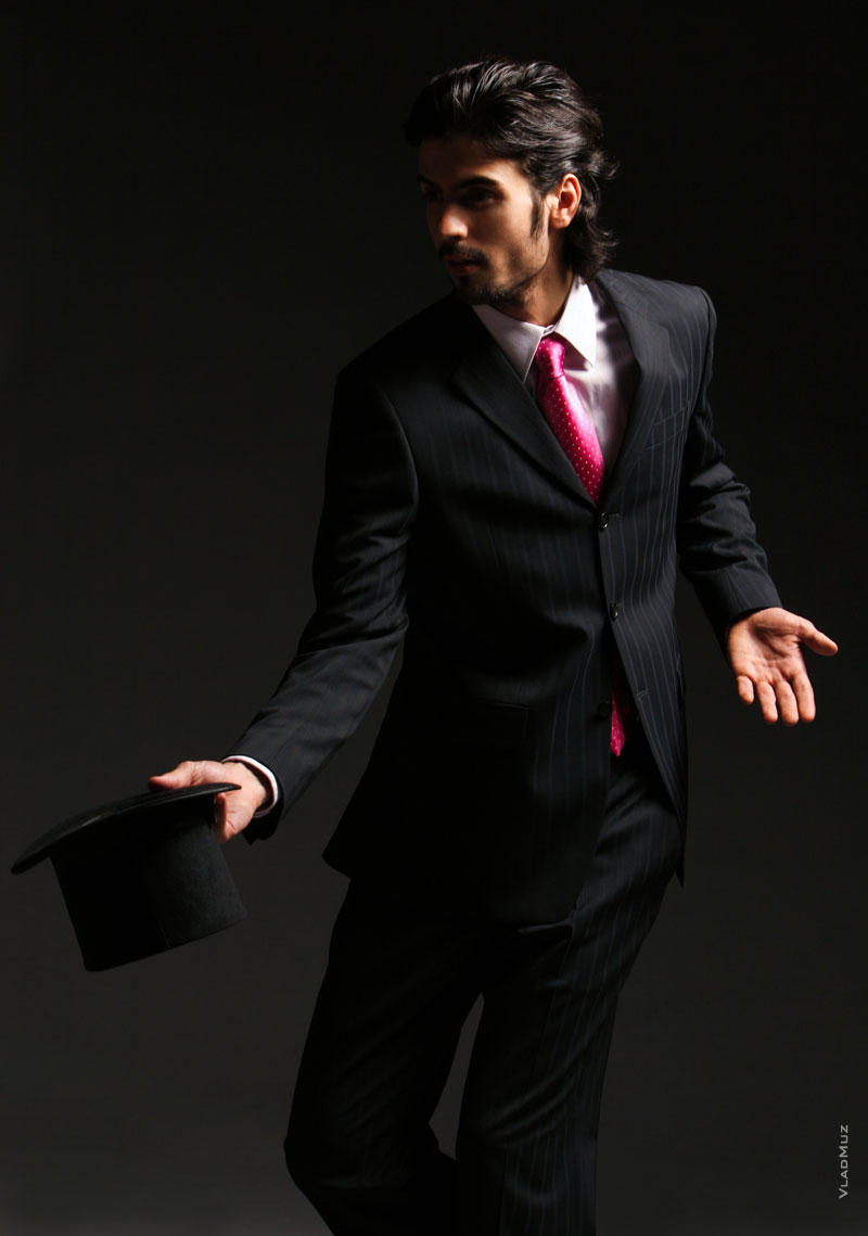 Динамичное студийное фото мужчины в костюме с галстуком, с цилиндром в руке