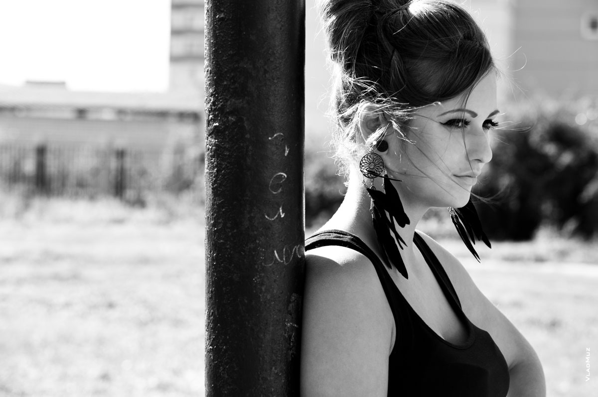 Черно-белый фотопортрет девушки с перьевыми сережками у столба