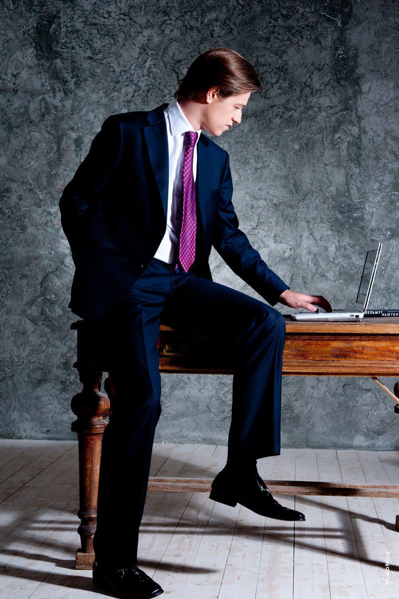Фото мужчины в деловом костюме, сидя на столе за ноутбуком, в полный рост