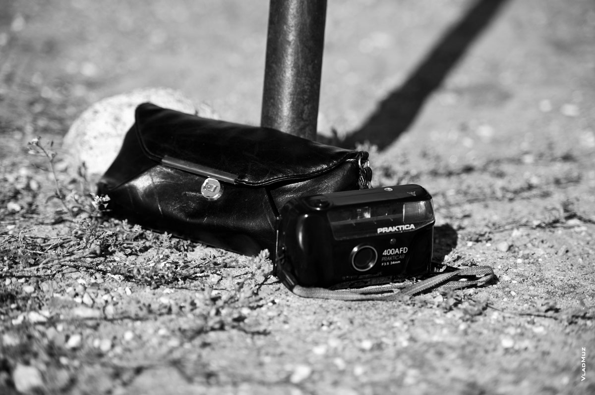 Черно-белое фото фотокамеры и женской сумочки на земле