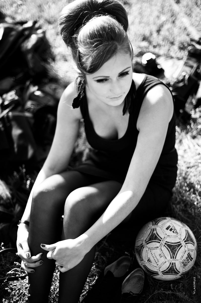 Фото красивой девушки, сидящей на земле, с футбольным мячом