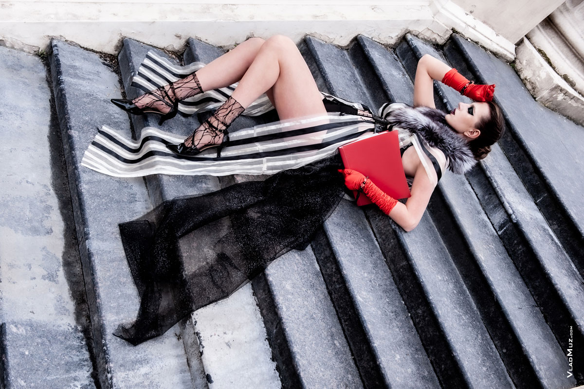 Фото девушки-модели в красных перчатках, лежа на лестнице в странной позе в полный рост, с красной папкой в руке