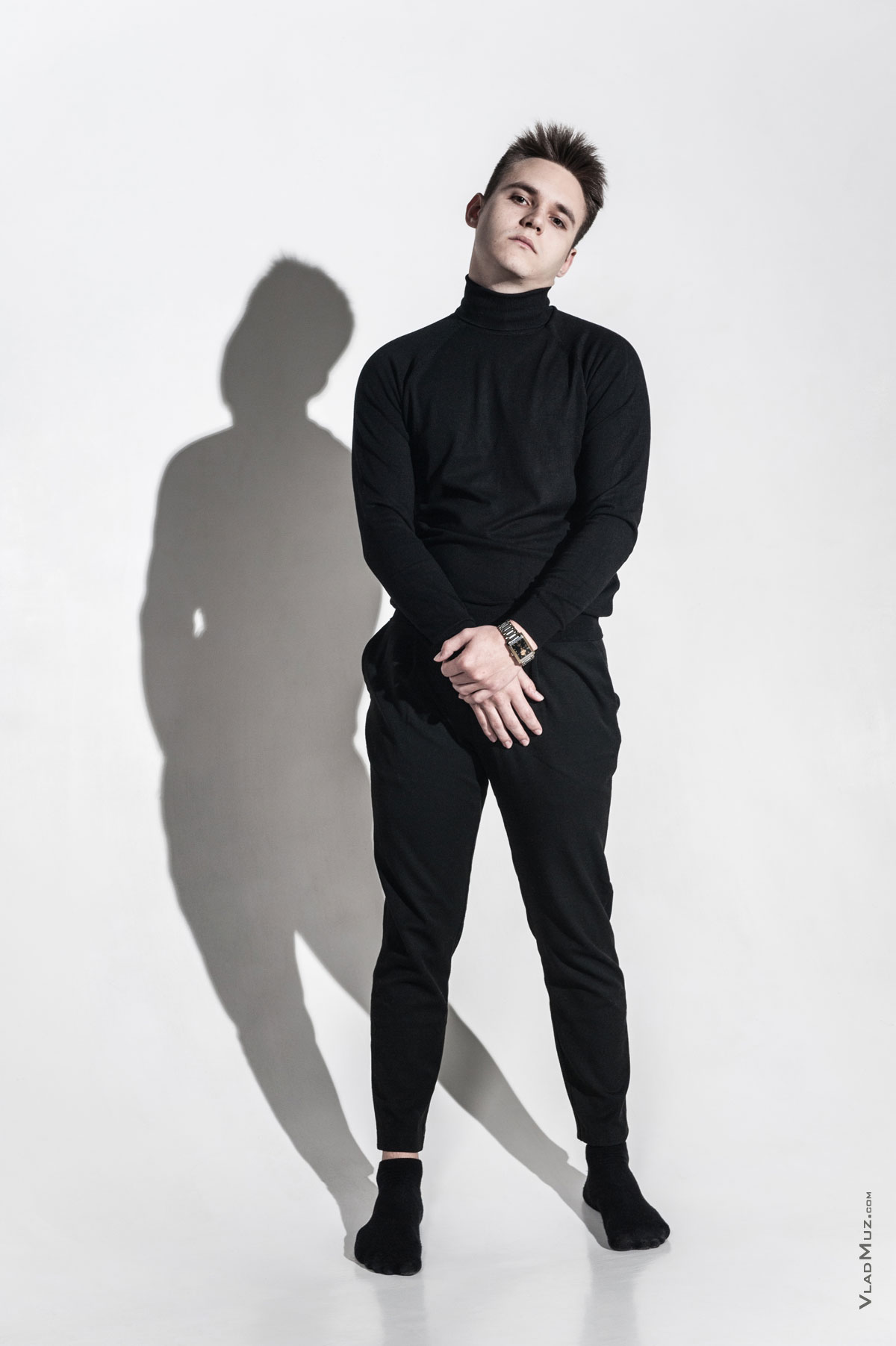 Фото мужчины-модели в черном в полный рост, на белой циклораме, с тенью на фоне