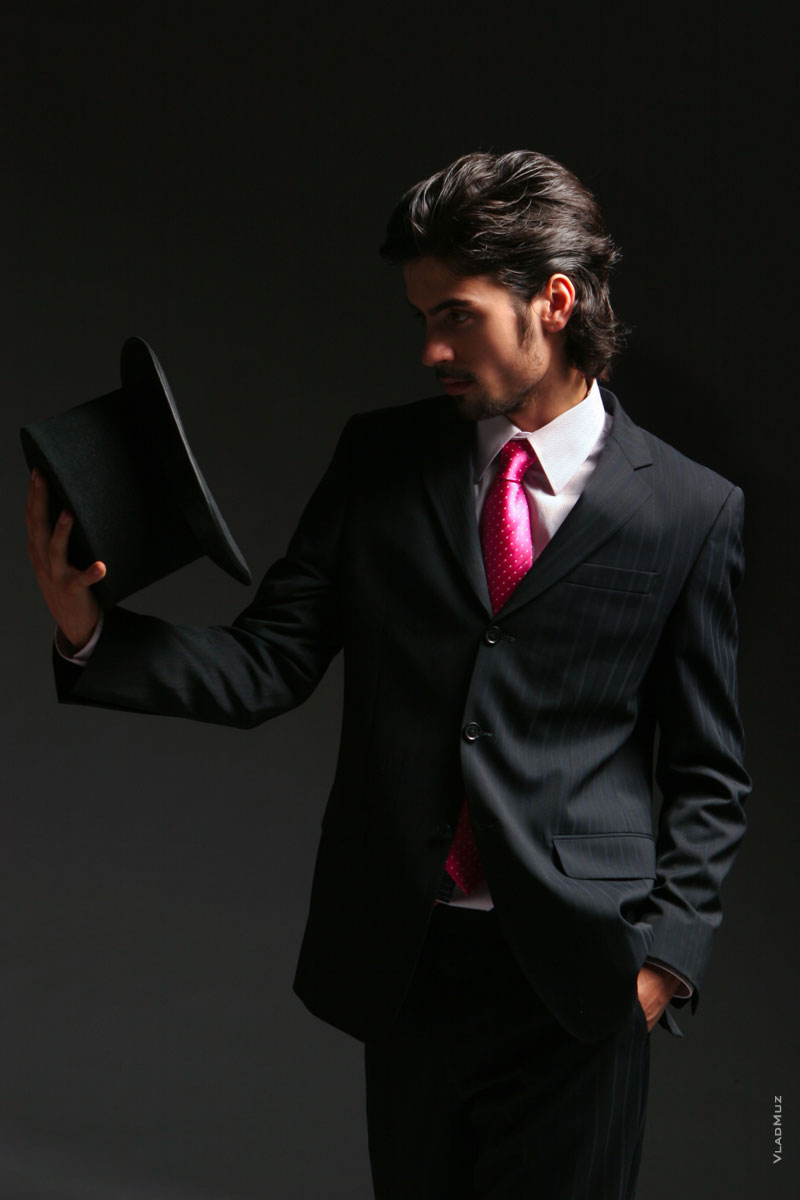 Поясное студийное фото мужчины в костюме с галстуком, с цилиндром в руке перед собой