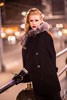 Фото девушки-модели в черном пальто с меховым воротником, в сильный ветер, на фоне ночного города